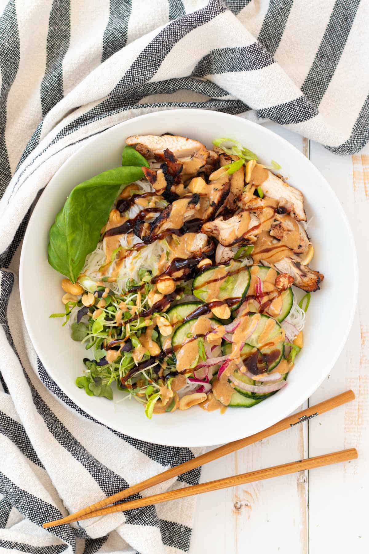 A white bowl of rice vermicelli with grilled chicken, quick pickled cucumber and red onion and all the garnishes.