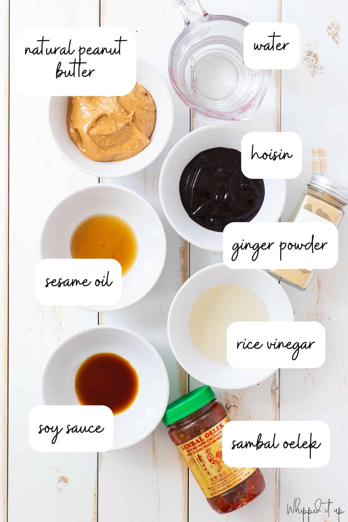 Ingredients to make peanut sauce measured out in white bowls on a white wood background.