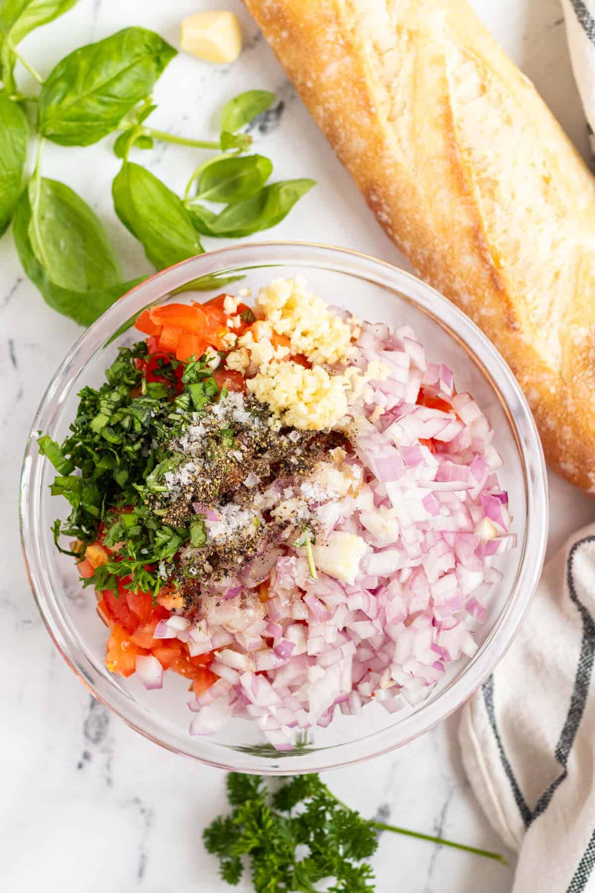 All bruschetta ingredients are piled in a glass bowl.