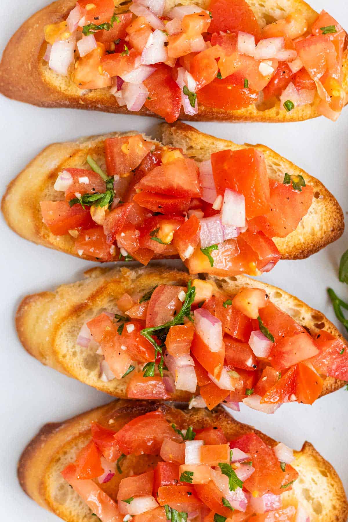 Topping toasted sourdough baguette slices with fresh bruschetta.
