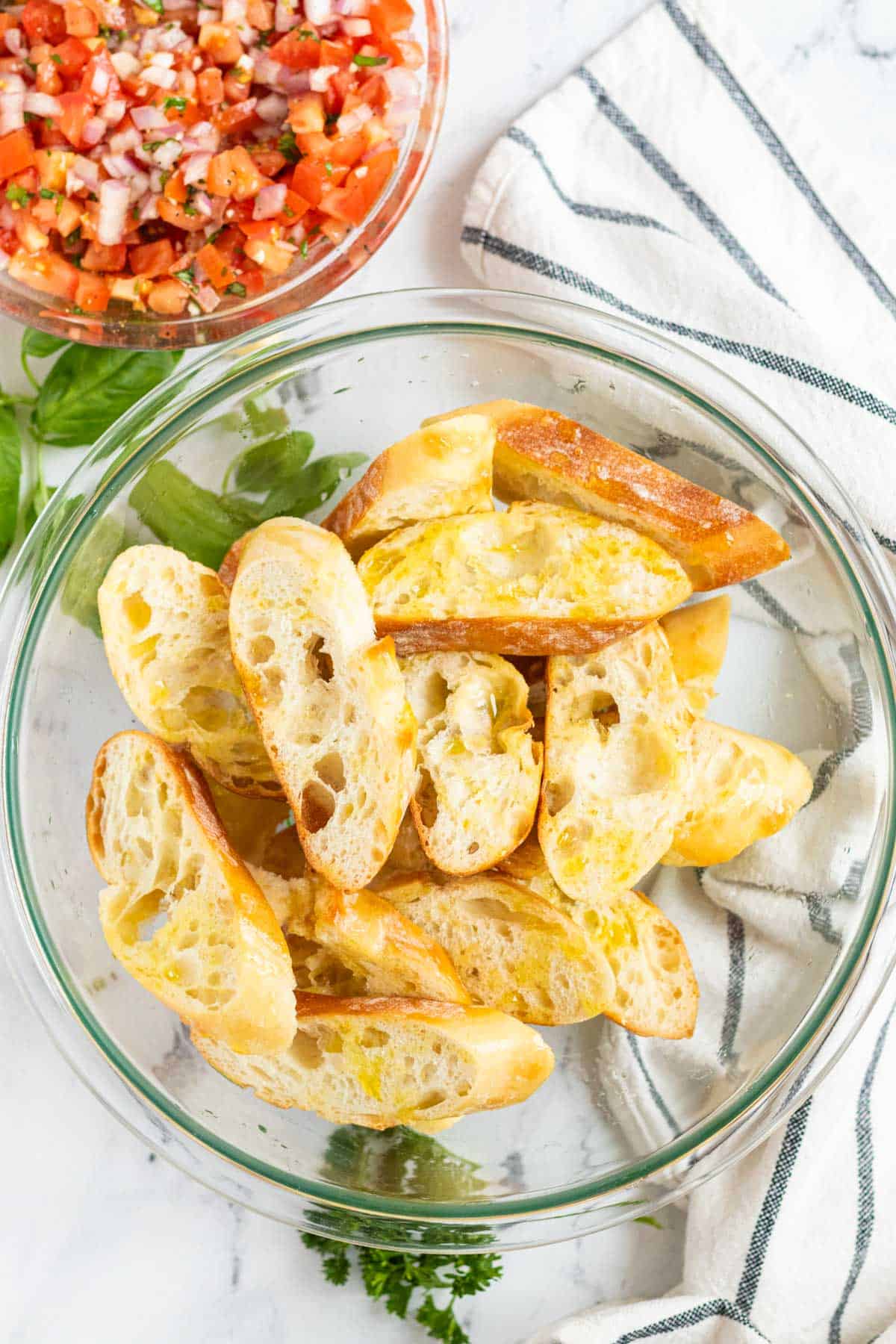 Tossing baguette slices with olive oil in a large glass bowl.