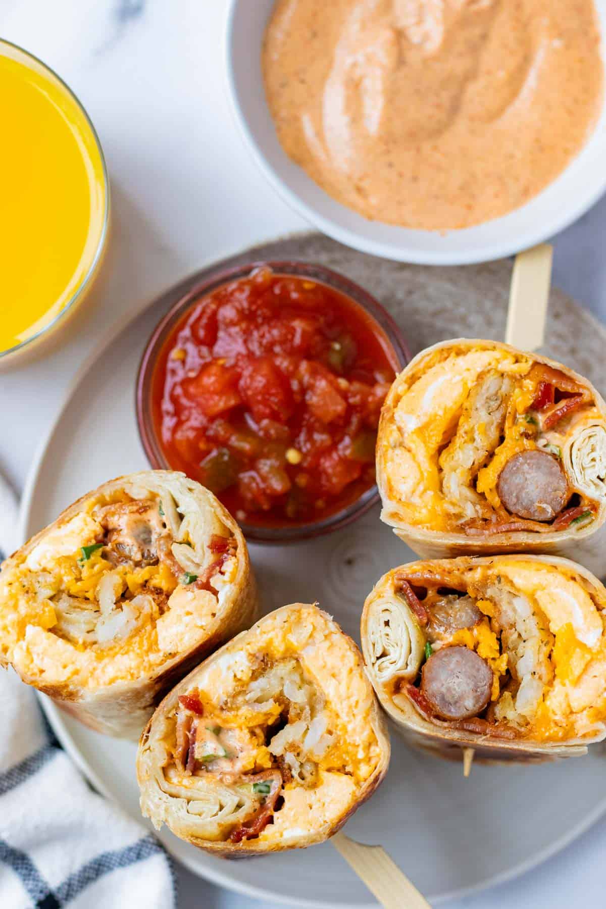 The ultimate fully loaded breakfast burritos bursting with sausage, bacon, eggs, cheese, and sriracha aioli on a plate.
