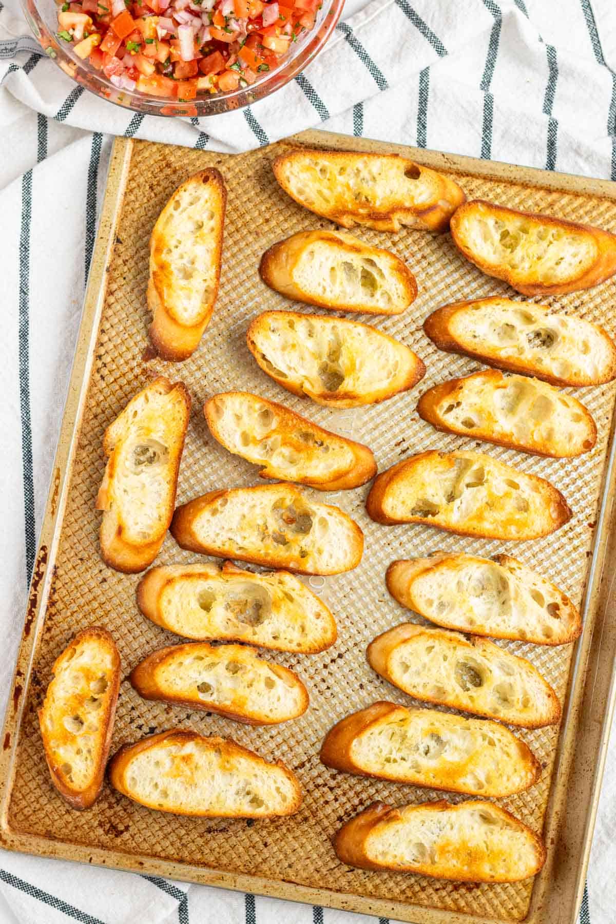 Golden toasted baguette slices on a gold baking tray.
