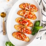 Five toasted baguette slices topped with tomato bruschetta on a white plate.