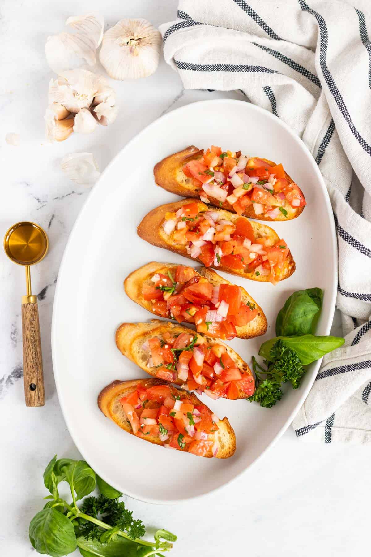 Five toasted baguette slices topped with tomato bruschetta on a white plate.