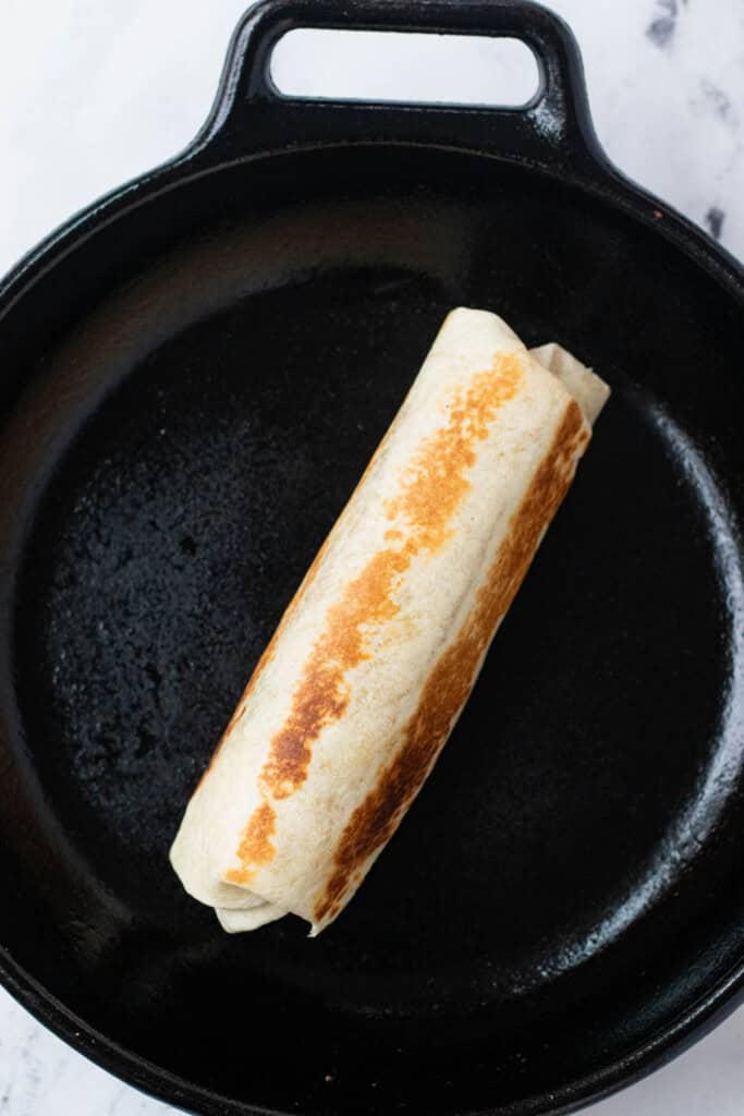 A fully loaded breakfast burrito rolled and toasted to golden brown in a cast iron pan.