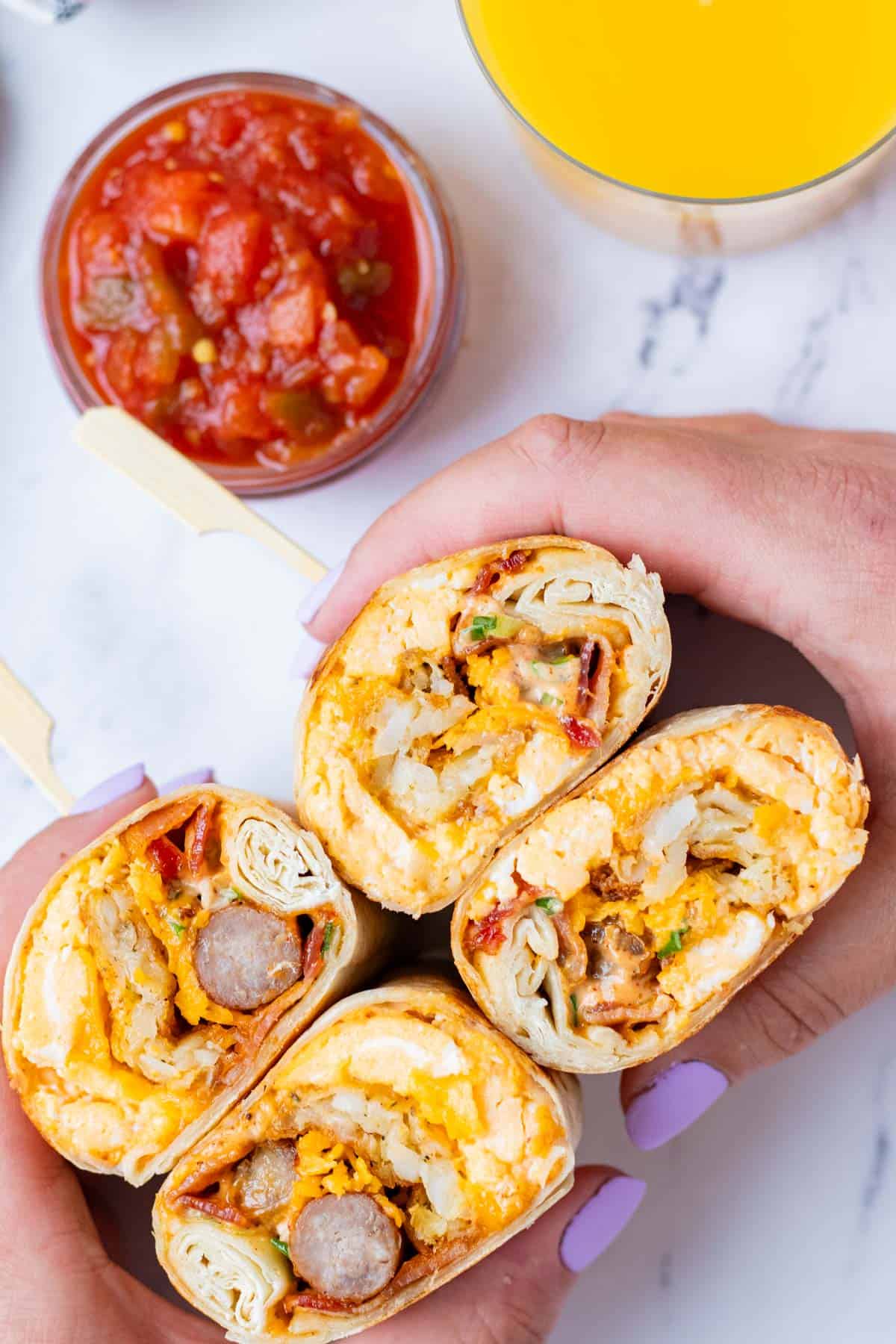 Hands holding two breakfast burritos that have been cut in half.