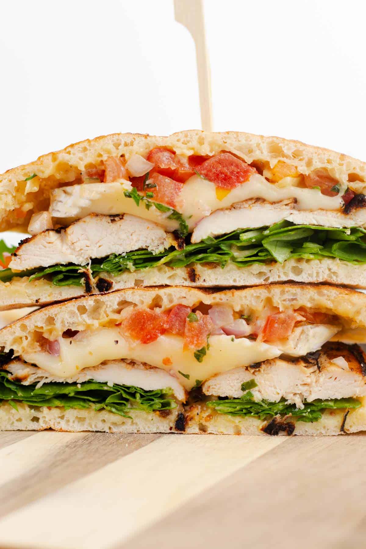 Close-up of a grilled chicken sandwich layered with melted brie, arugula, and fresh tomato bruschetta.