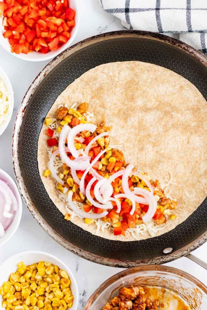 Filling a tortilla with quesadilla toppings in a frying pan.