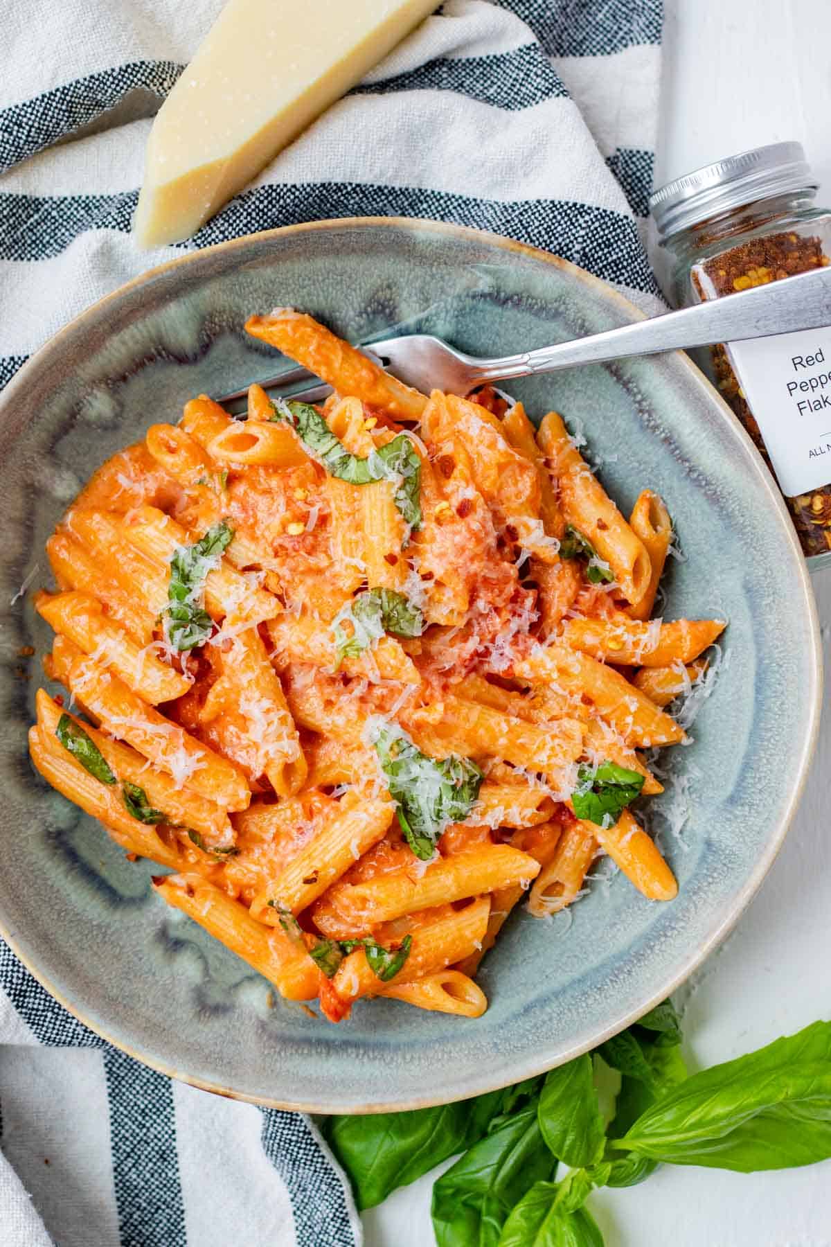 Finished penne alla vodka in a blue bowl with creamy vodka sauce, parmesan cheese, and fresh basil.