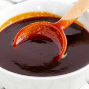 Thick, glossy brown sauce in a white bowl with a wooden spoon lifting a spoonful to show its smooth consistency.