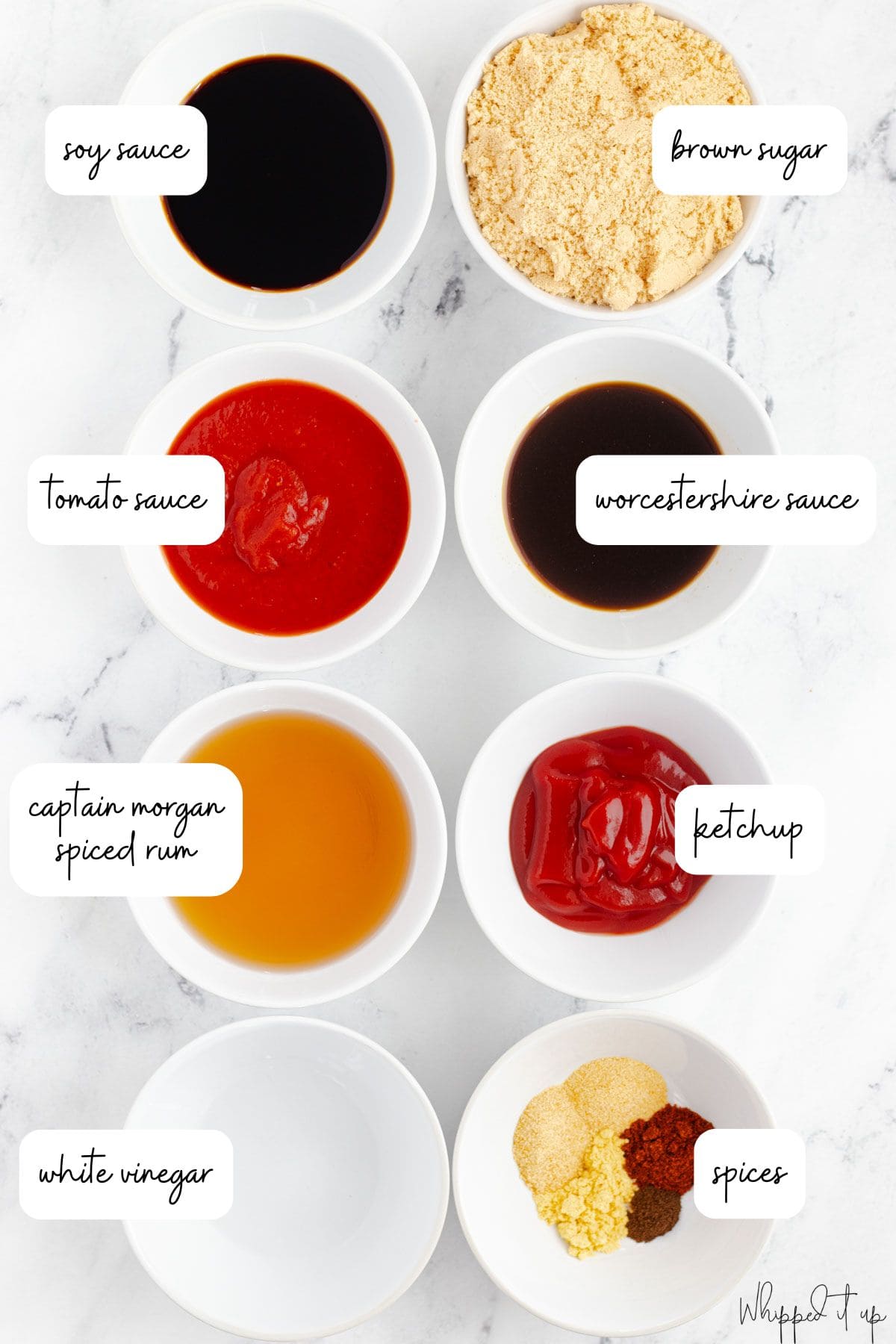 Ingredients to make barbecue sauce are measured into white bowls on a marble countertop.