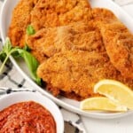 Crispy golden chicken cutlets served with lemon slices and marinara sauce for dipping.