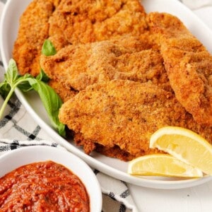 Crispy golden chicken cutlets served with lemon slices and marinara sauce for dipping.