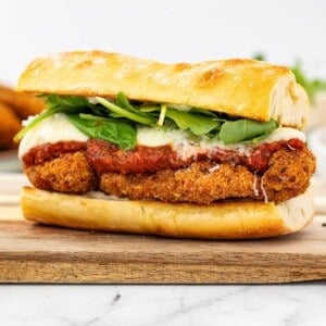 A fully loaded chicken parmesan sandwich on a wooden board showing all the layers.