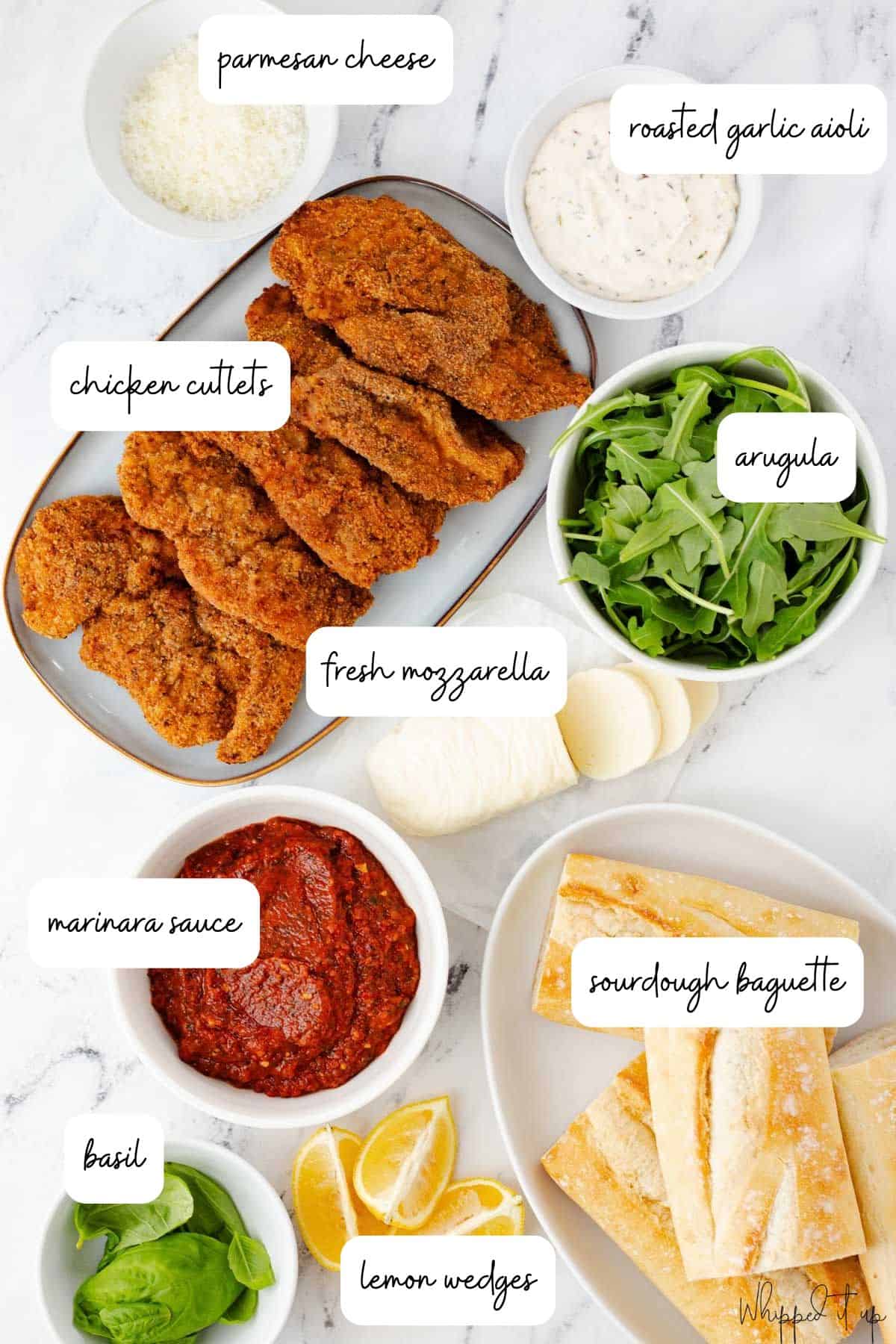 Ingredients to make chicken parmesan sandwiches on a white marble background.