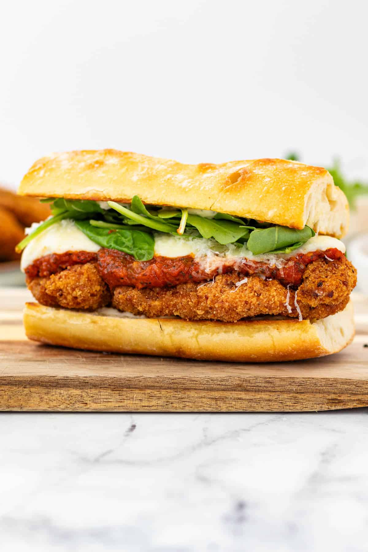 A fully loaded chicken parmesan sandwich on a wooden board showing all the layers.