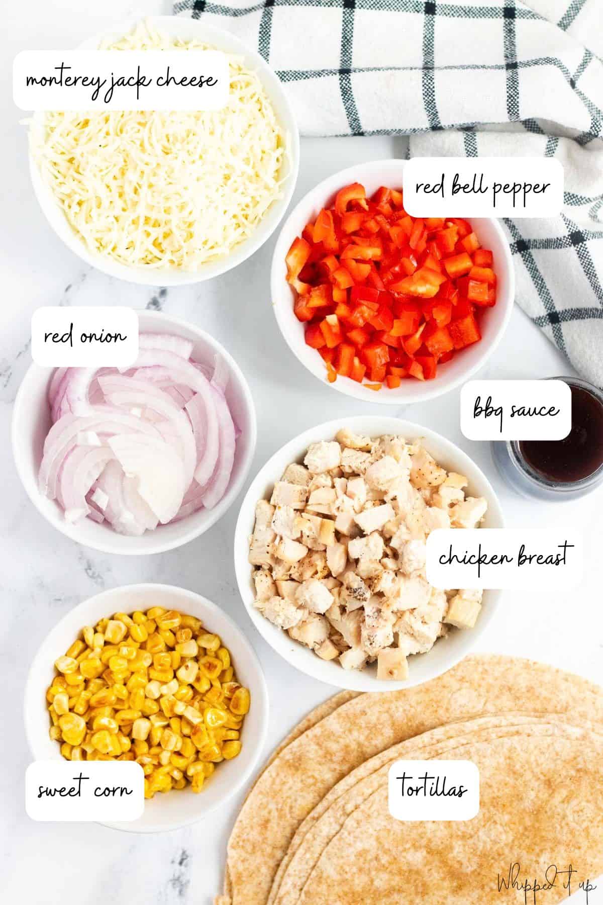 Ingredients to make barbecue chicken quesadillas are measured out into white bowls on a white background.
