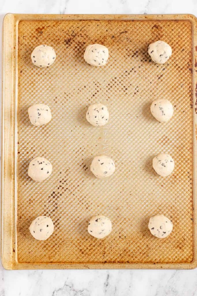 Cookie dough is rolled into balls and evenly spaced on a cookie sheet.