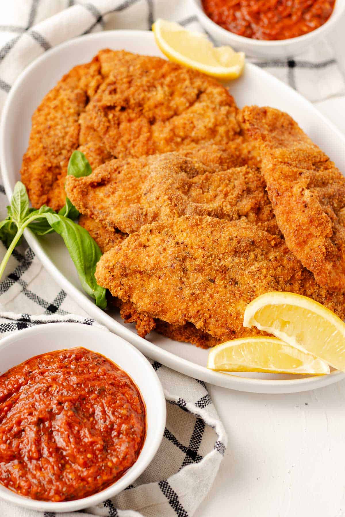 Crispy golden chicken cutlets served with lemon slices and marinara sauce for dipping.