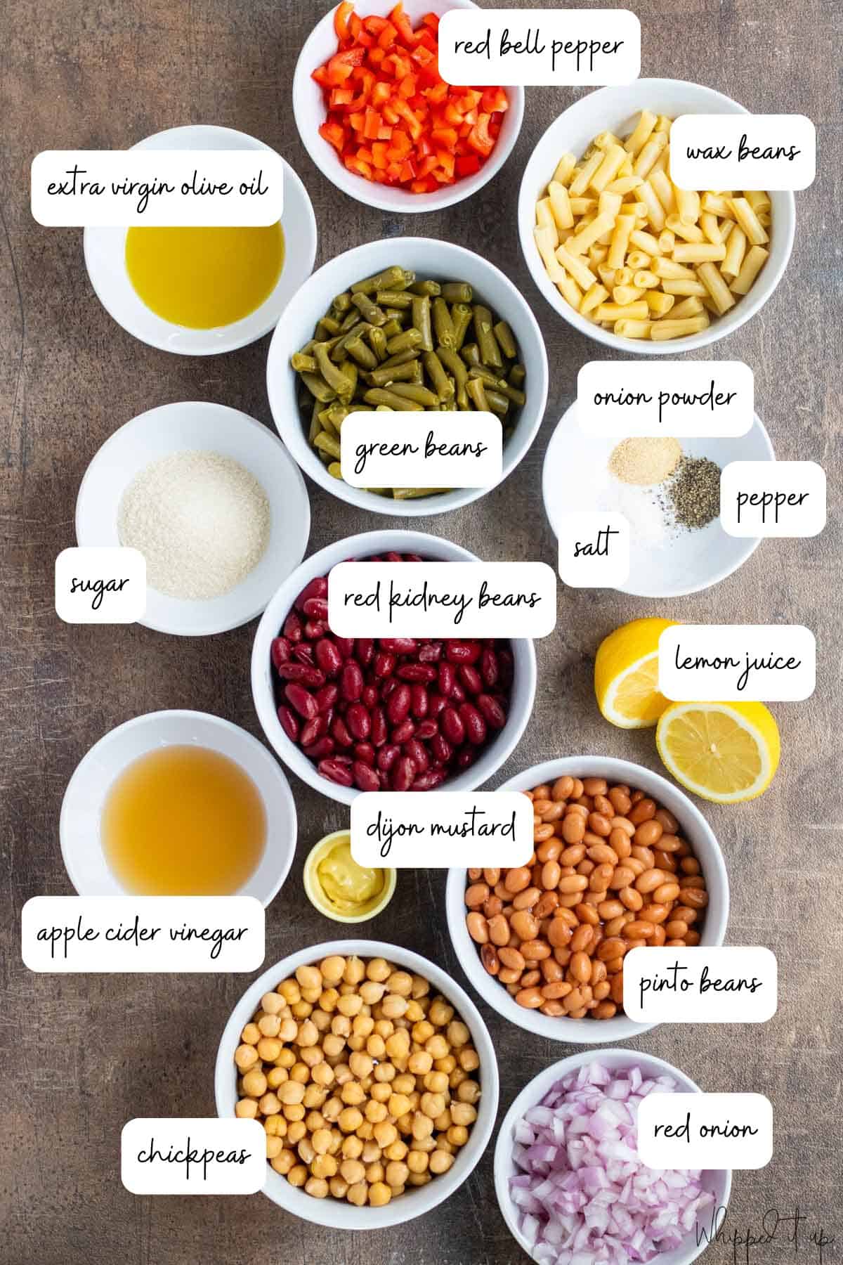 Ingredients to make bean salad are laid out in white bowls on a concrete background.