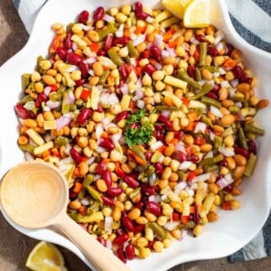 Dense bean salad in a white serving dish with a wooden spoon on the side.