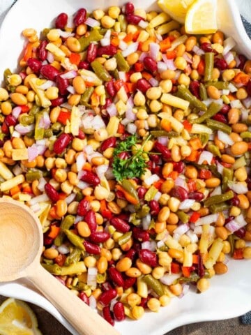 Dense bean salad in a white serving dish with a wooden spoon on the side.