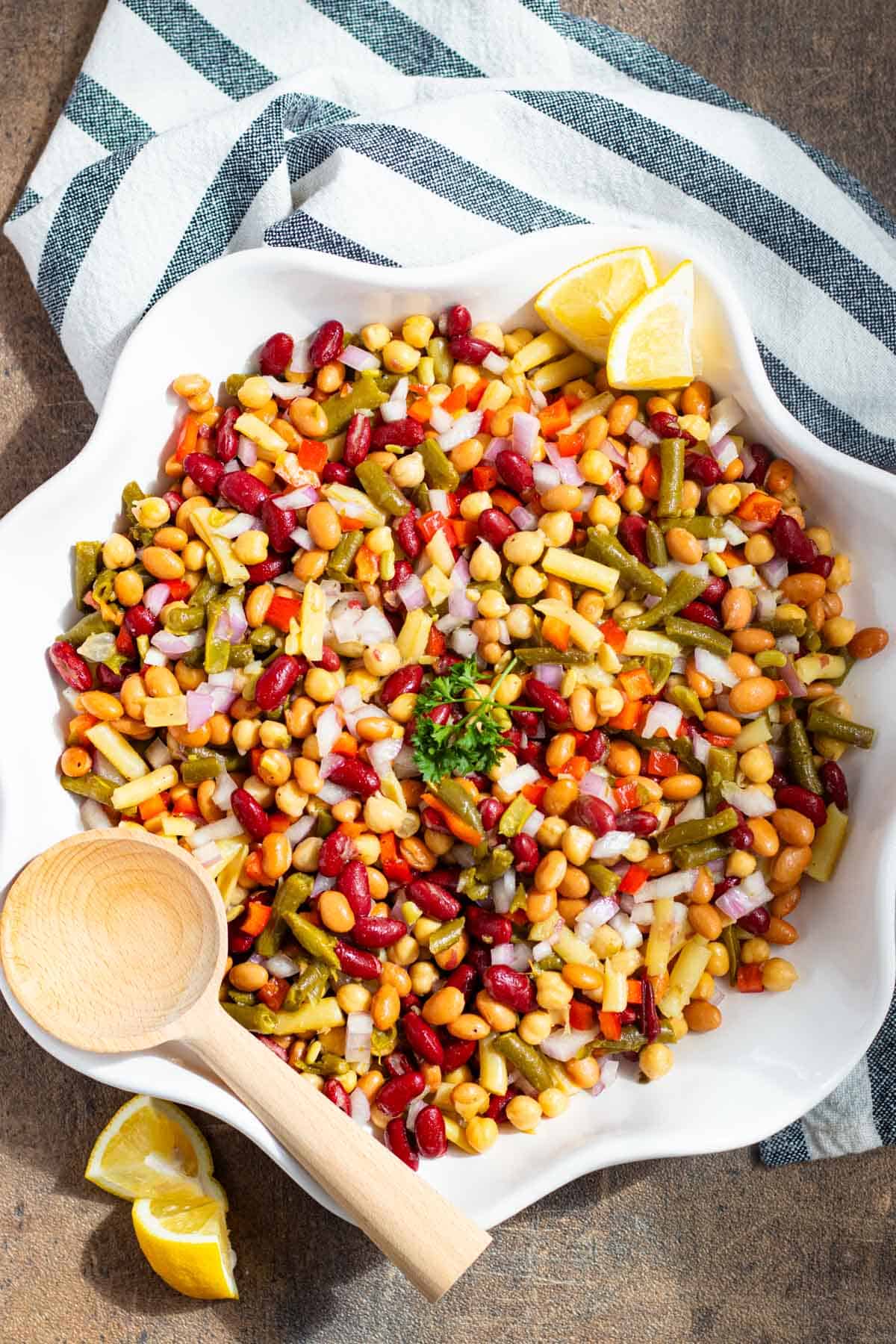 Dense bean salad in a white serving dish with a wooden spoon on the side.