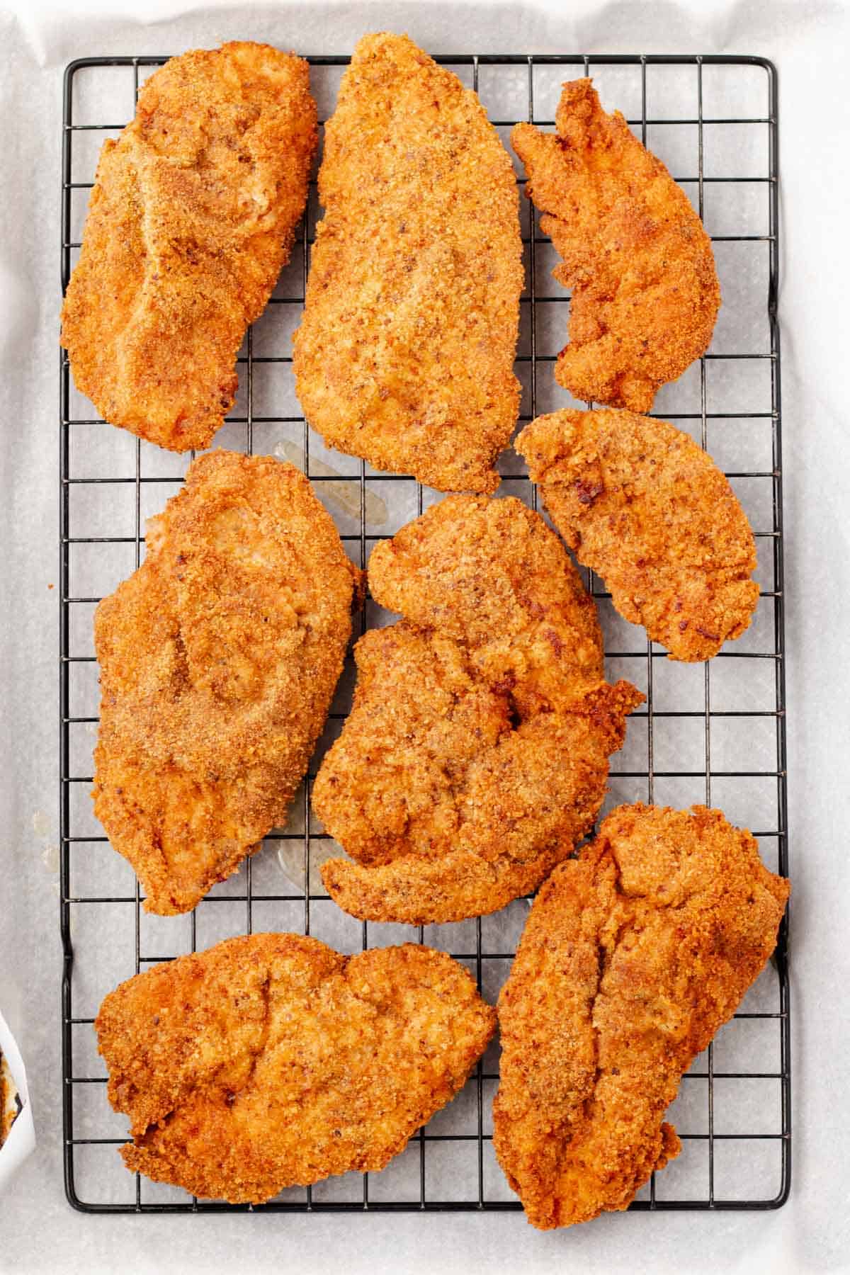 Fried chicken cutlets on a wire cooling rack after frying and baking.