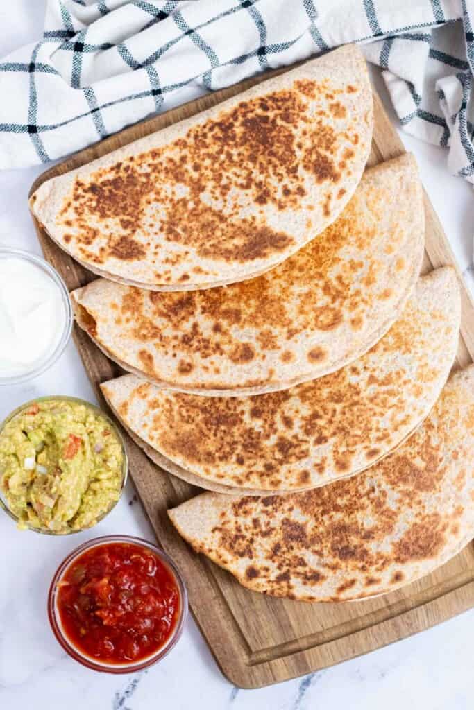 Uncut, grilled chicken quesadillas on a cutting board with dipping sauces on the side.