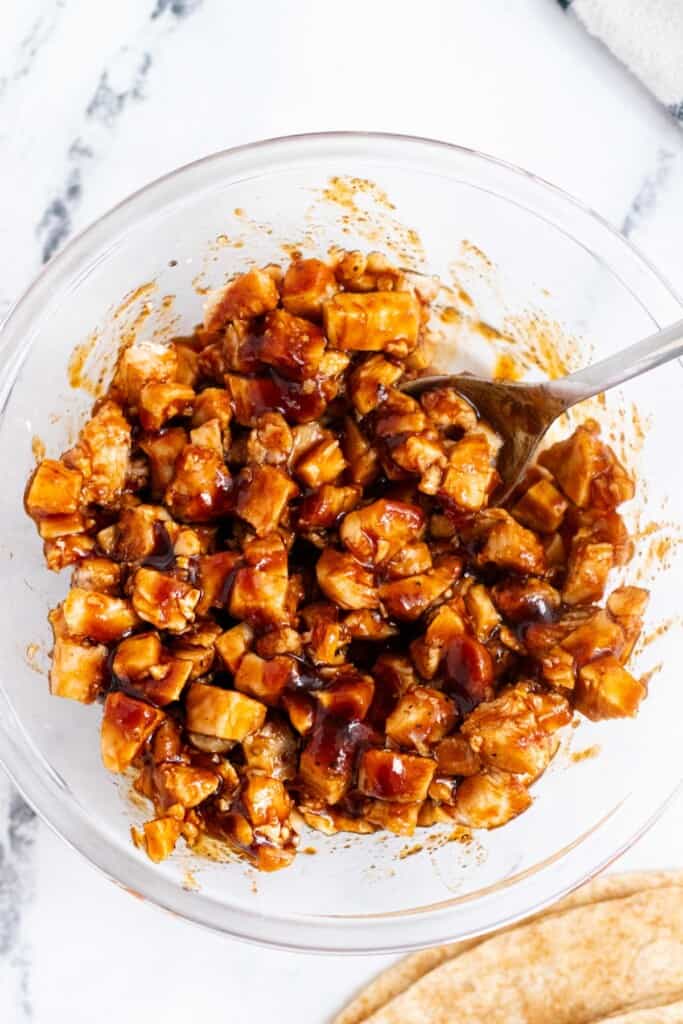 Mixing the cooked chicken with barbecue sauce in a glass bowl.