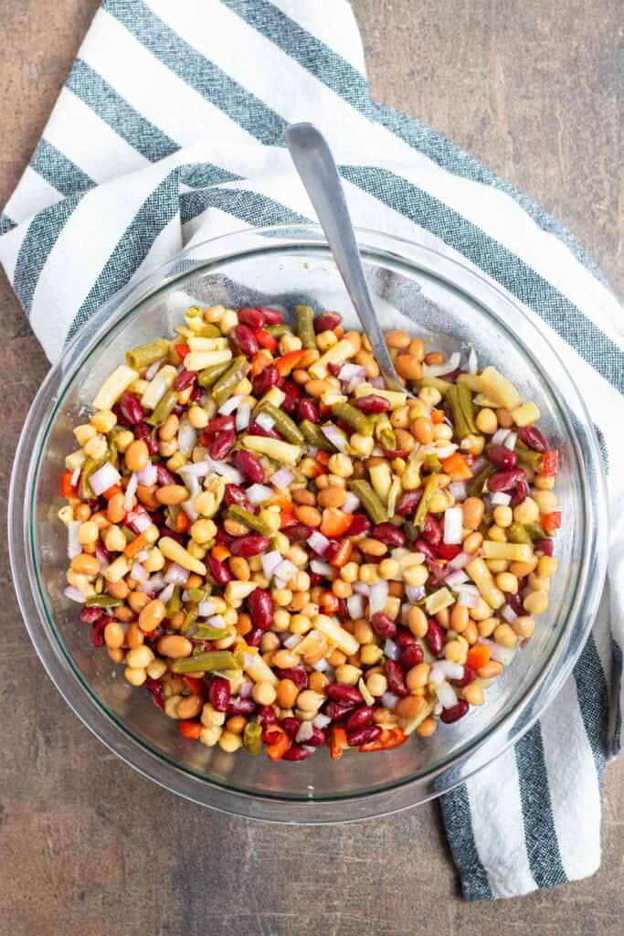 Stirring the bean salad in a mixing bowl with a serving spoon.