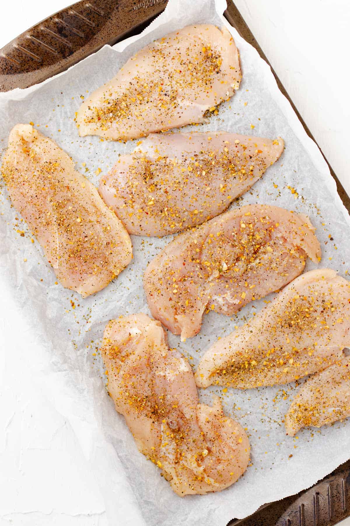 Pressing spices into raw chicken breasts before breading them.