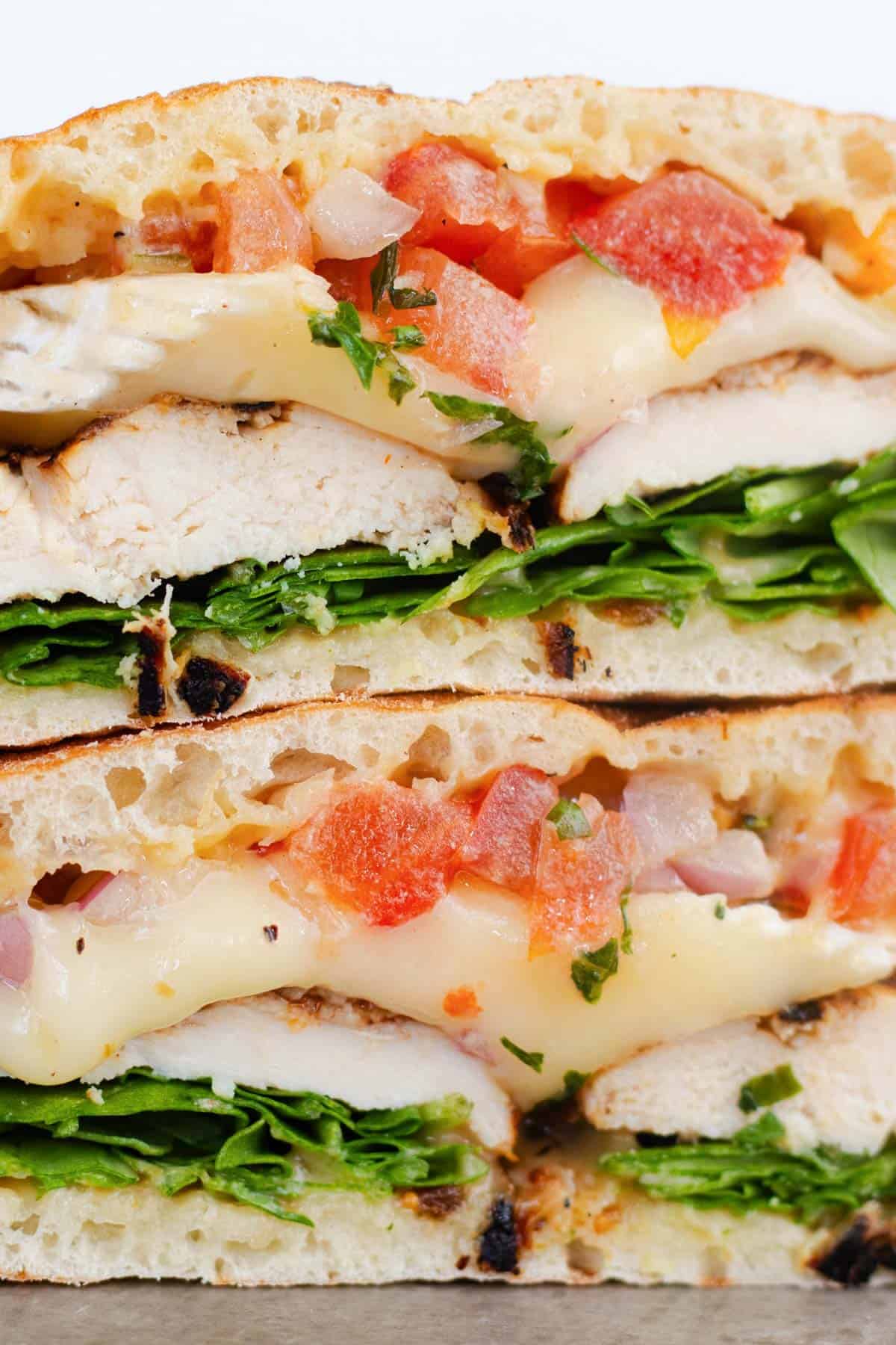 Close up cross section of grilled chicken brie sandwich with melted brie, arugula, and tomato bruschetta.