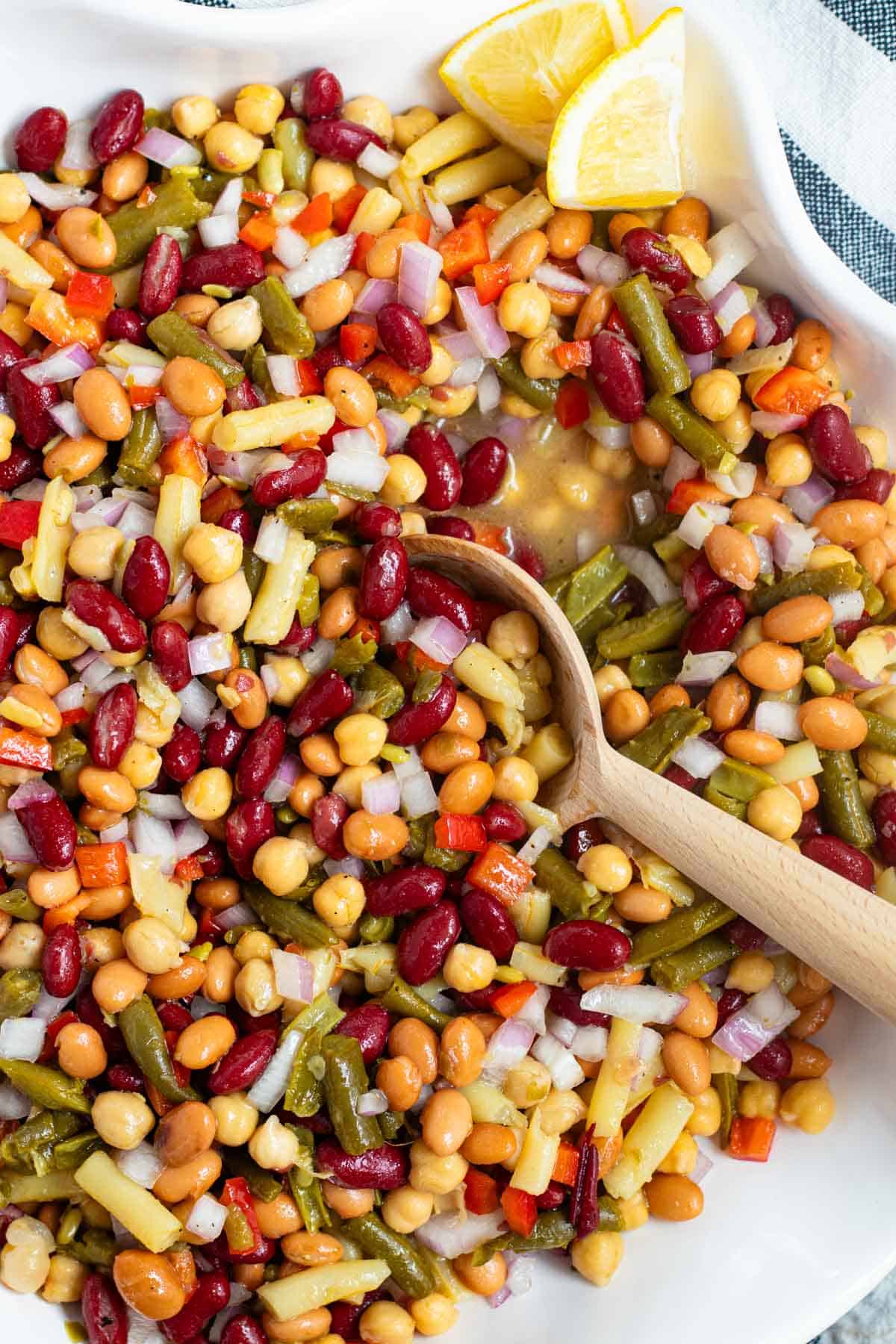 A wooden serving spoon scooping up bean salad from a white serving bowl.
