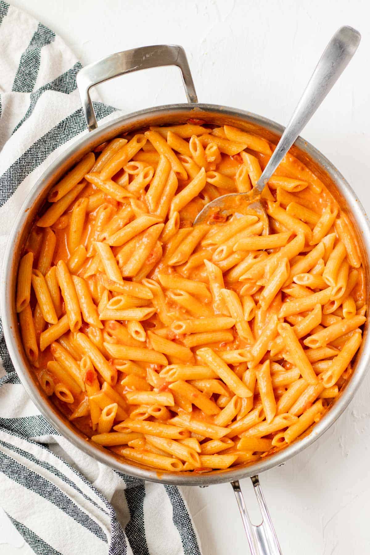 Stirring cooked penne pasta into the vodka sauce.