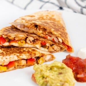 BBQ chicken quesadilla triangles cut on a white plate with salsa, guacamole, and sour cream dipping sauces on the side.