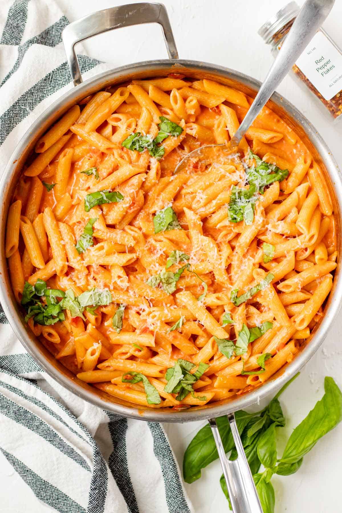 Topping the vodka sauce penne with fresh basil and parmesan cheese.