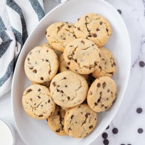 An oval white serving tray piled with vegan chocolate chip cookies.