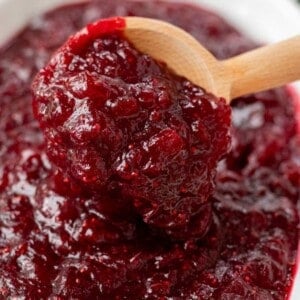 A spoonful of thick, glossy whole berry cranberry sauce on a wooden spoon.