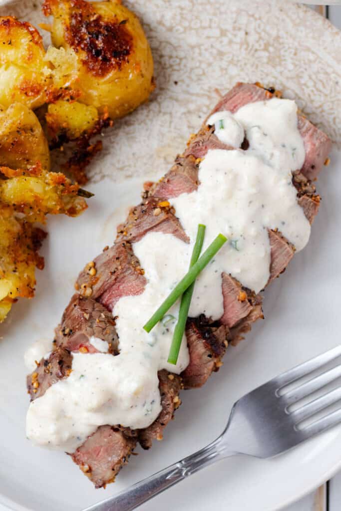 Horseradish sauce poured on top of a sliced medium-rare steak.