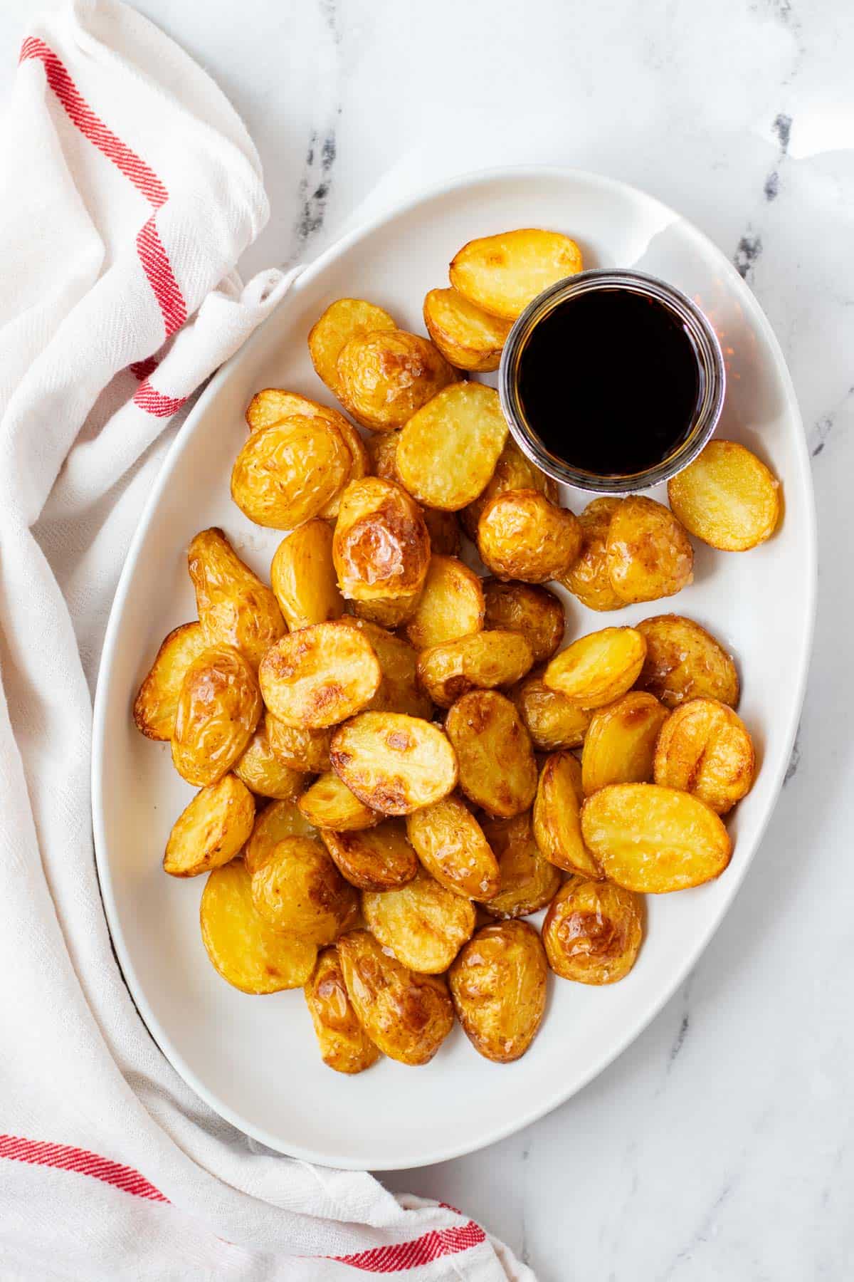 Salt and vinegar roasted potatoes on a white plate with a side of malt vinegar.