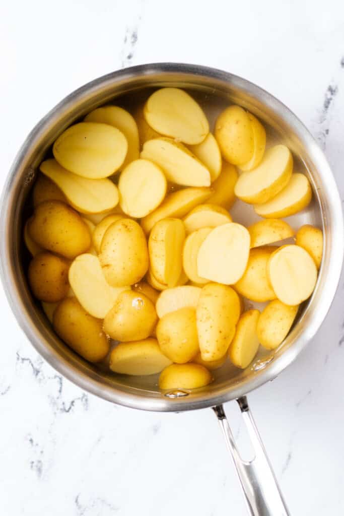 A saucepan filled with water, vinegar, salt, and halved potatoes.