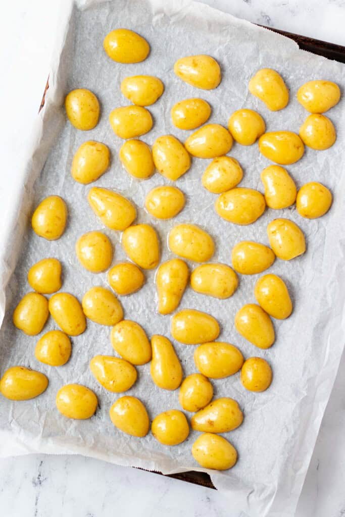 Parboiled potatoes face down on a baking sheet with a piece of parchment paper.