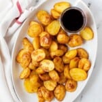 Salt and vinegar roasted potatoes on a white plate with a side of malt vinegar.