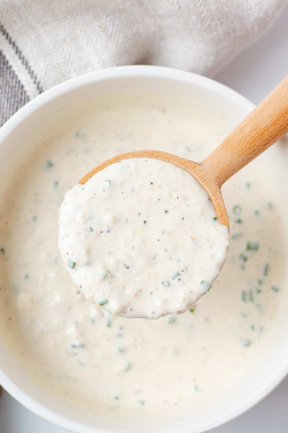 A wooden spoon full of horseradish sauce over a bowl.