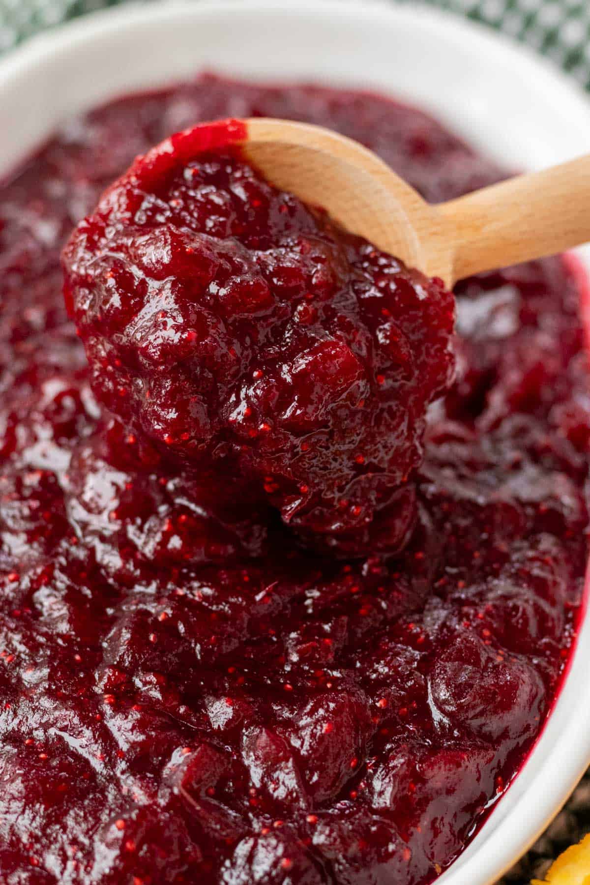 A spoonful of thick, glossy whole berry cranberry sauce on a wooden spoon.